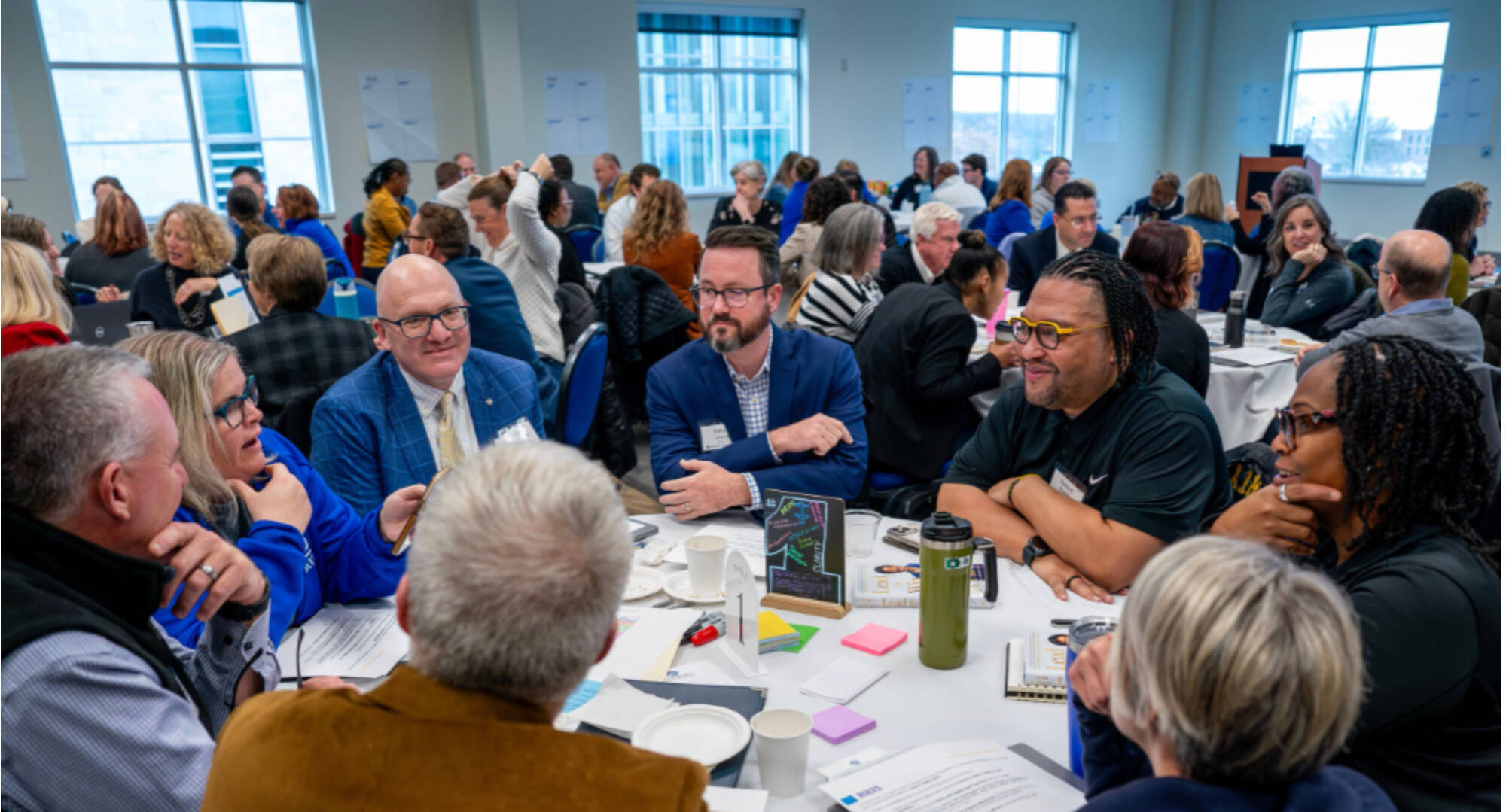 Group of people sitting at a table with sticky notes and pens on it having a discussion